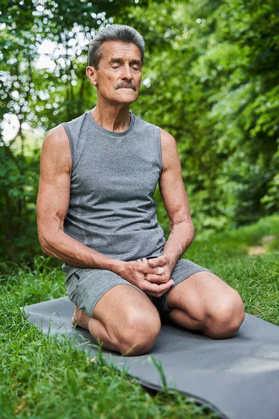 Мужчина сидит на согнутых ногах у коврика для йоги и держит глаза закрытыми. — стоковое фото