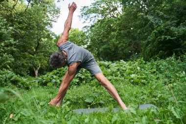 Ormanda egzersiz yaparken vücudunu esneten ve esnek hisseden bir adam.
