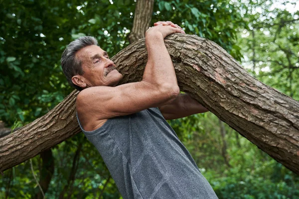 Uomo anziano che tiene tronco d'albero e fa tirare su mentre si allena nella foresta — Foto Stock