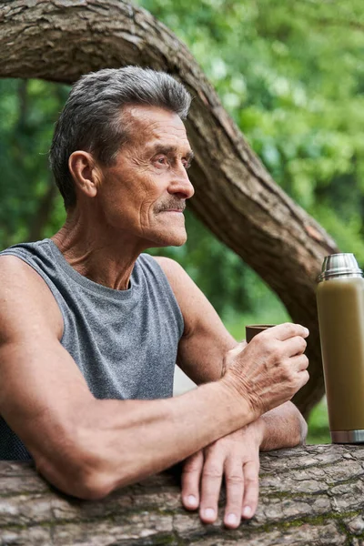 Man looking at the distance and drinking hot tea while relaxing after workout — Stock Photo, Image