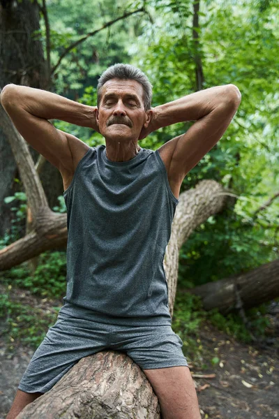 Uomo con gli occhi chiusi che tiene le mani dietro la testa e siede all'albero — Foto Stock