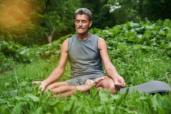 Человек практикующий йогу и занимающийся упражнениями ardha padmasana, сидя в позе лотоса — стоковое фото