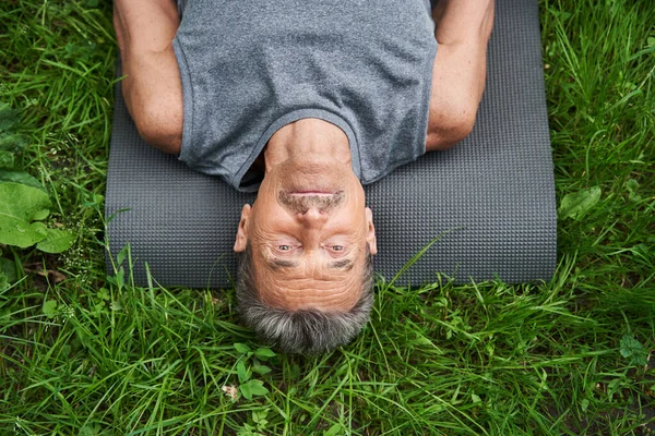 Человек, лежащий на коврике для йоги на траве после упражнений и расслабления — стоковое фото