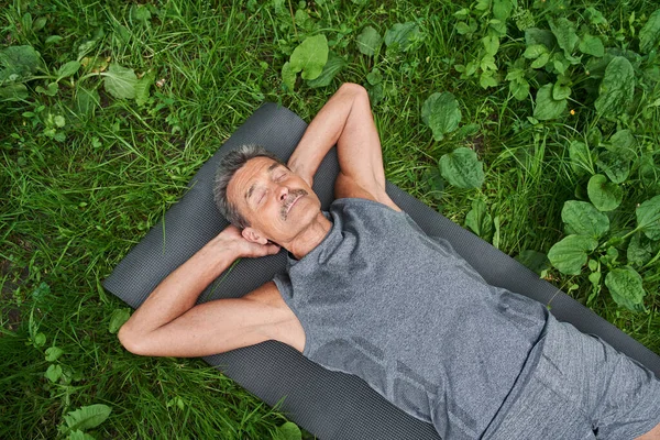 Мужчина лежит на спортивном коврике, расслабляется в позе савасаны после тренировки на свежем воздухе — стоковое фото