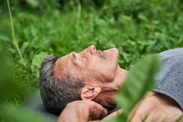 Зрелый человек делает расслабляющую позу йоги, лежа на коврике на природе — стоковое фото