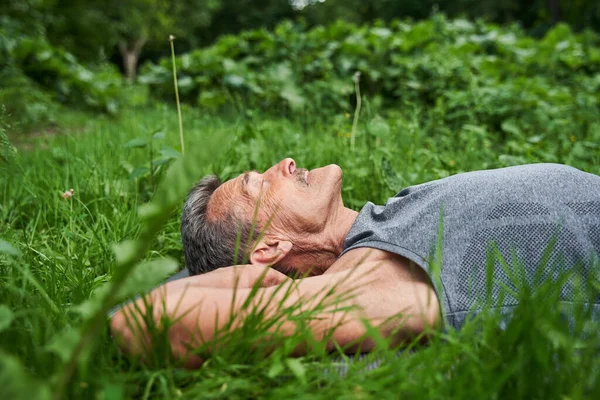 Hombre acostado en la esterilla de yoga en la hierba después de ejercicios y relajarse —  Fotos de Stock