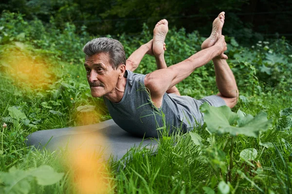 Homme tenant ses jambes avec ses mains tout en étant allongé au tapis de yoga à la pose flexible — Photo