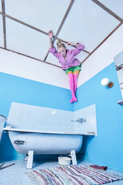 Meisje draagt heldere kleren liggen aan het plafond hoofd over hakken in de badkamer — Stockfoto