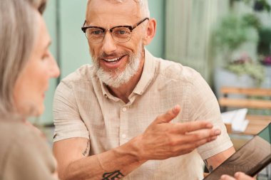 Man telling something to his beloved wife while holding tablet during the sitting