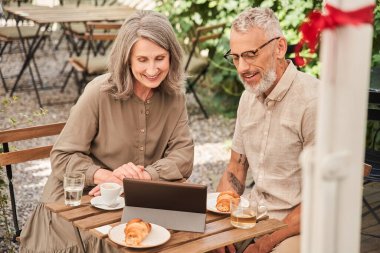 Married woman and man sitting at the cafe and holding tablet while looking at it
