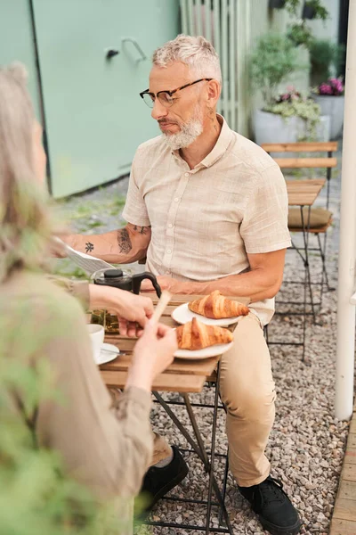 Man wearing glasses looking at the newspaper while discussing news with his lovely wife — Stockfoto