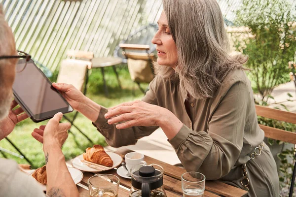 Senior woman giving digital tablet to her lovely husband while sitting — Stockfoto