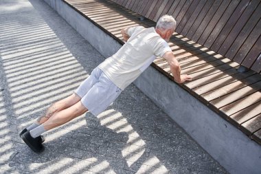 Concentrated man making push ups and holding at the bench while exercising