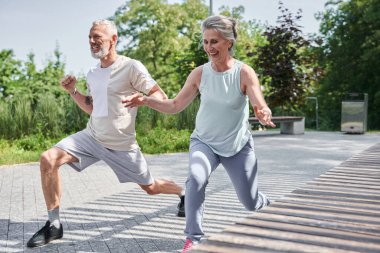 Senior married couple making lunges while training at the morning at the fresh air