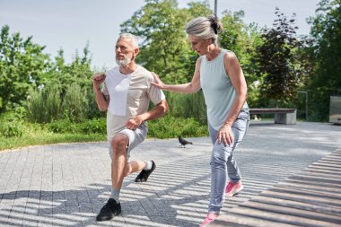 Senior married couple making lunges while training at the morning at the fresh air