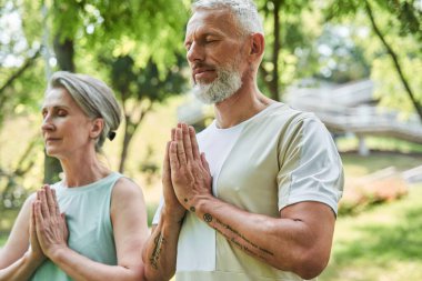 Serene mature married couple enjoying meditation around the trees