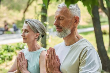 Serene mature married couple enjoying meditation around the trees