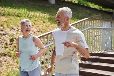 Happy senior couple running with delight at the summer park and trying to keep body fit