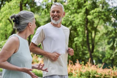 Beloved couple in good shape jogging at the summer park and looking at each other
