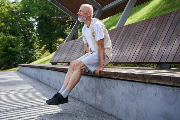 Старший сидит на деревянной скамейке и смотрит в сторону, когда отдыхает. — стоковое фото