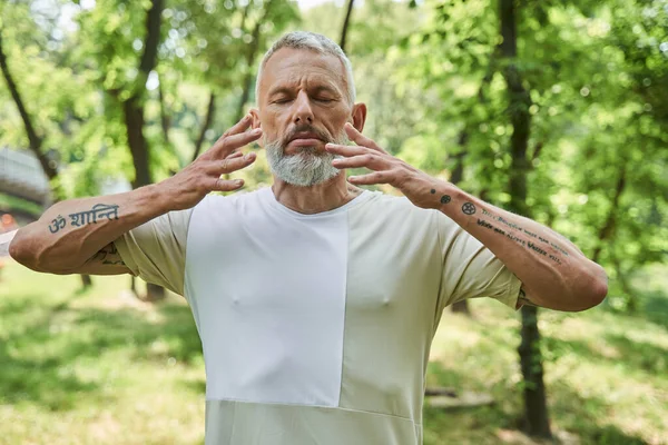 Anciano manteniendo los ojos cerrados y haciendo ejercicio respiratorio mientras disfruta — Foto de Stock