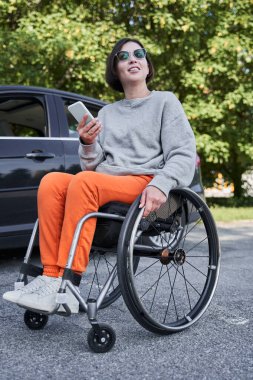 Handicapped woman sitting at the special armchair and holding her smartphone