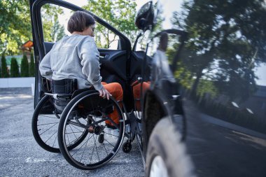 Young girl with lower body disability switches position from the wheelchair into the car clipart