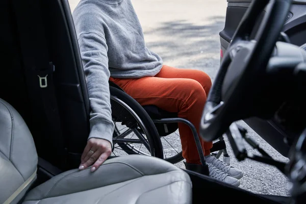 Young disabled female getting out from the car in her wheelchair after the road