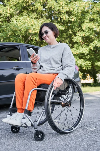 Fille avec un handicap du bas du corps assis au fauteuil roulant près de sa voiture et vérifier les messages — Photo
