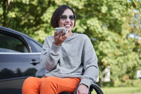 Woman sitting at the wheelchair and recording voice message at her mobile phone — Φωτογραφία Αρχείου