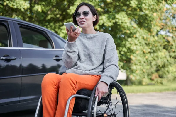 Femme handicapée assise au fauteuil roulant et enregistrant un message vocal sur son portable — Photo