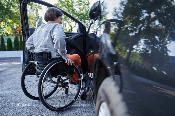Молодая девушка с ограниченными физическими возможностями переключается с инвалидного кресла на автомобиль — стоковое фото