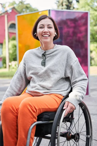 Woman with lower body disability wearing earphones sitting at the special armchair