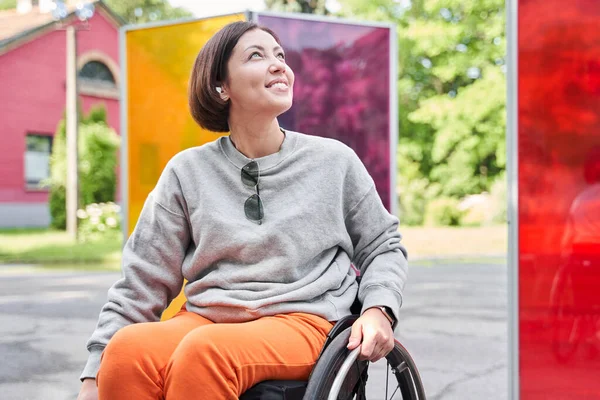 Femme portant des écouteurs regardant loin avec le sourire de plaisir tout en étant assis au fauteuil roulant — Photo