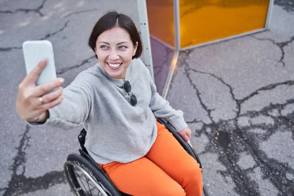 Femme handicapée faisant selfie tout en étant assis au fauteuil roulant pendant la marche — Photo