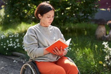 Calm woman sitting at the wheelchair and writing something at her notebook