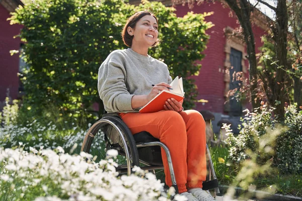 Femme handicapée du bas du corps assise au fauteuil roulant et réfléchissant en écrivant — Photo