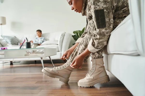 Жінка в військовій формі зав'язує шнурки взуття, сидячи на дивані — стокове фото