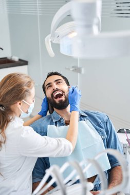 Dişçi koruyucu maske takıyor. Çok ırklı erkek müşterisinin yanında duruyor.