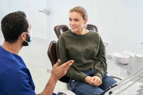 Vista posterior del dentista masculino en el consultorio dental hablando con la paciente rubia femenina — Foto de Stock