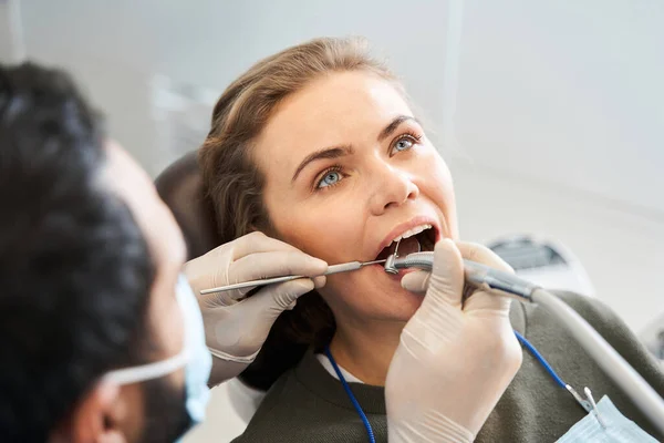 Dentista cuidadoso con guantes de goma tratando a la joven rubia — Foto de Stock