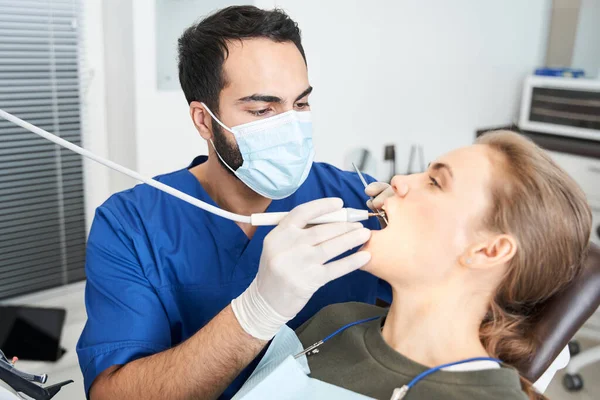 Noggrann tandläkare i skyddande mask behandla ung blond kvinna — Stockfoto