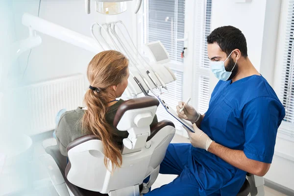 Dentista mostrando el papel a una cliente sonriente satisfecha — Foto de Stock