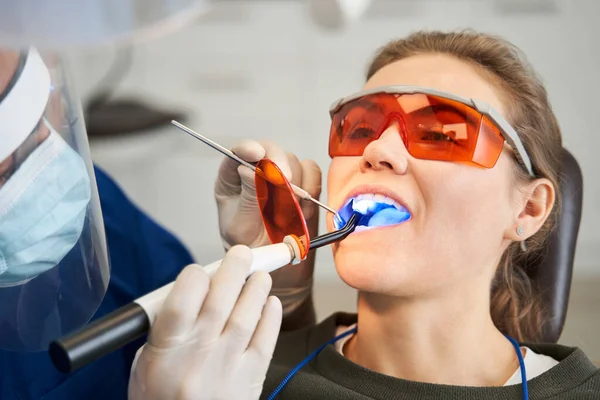 Dentista usando la lámpara UV de curado dental en los dientes del paciente — Foto de Stock