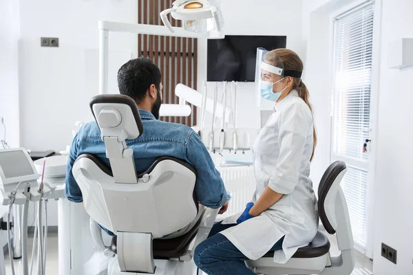 Dentista en máscara protectora examinando a su paciente masculino — Foto de Stock