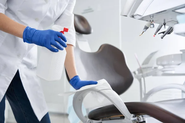 Dentista usando desinfectante antiséptico y limpiando el sillón estomatológico —  Fotos de Stock