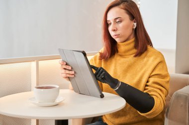 Kafedeki masada dijital tablet kullanan protez kollu bir kadın.