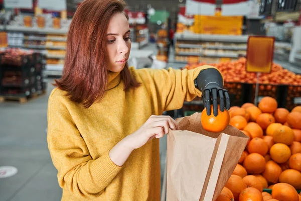 Cliente con brazo de prótesis eligiendo naranjas en el mercado de frutas —  Fotos de Stock