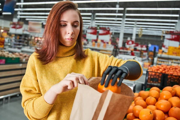 Cliente con brazo de prótesis eligiendo naranjas en el mercado de frutas —  Fotos de Stock