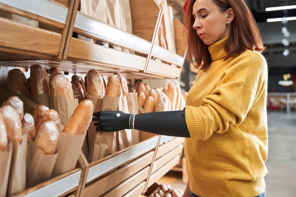 Žena s implantovanou paží dotýkající se chleba v obchodě — Stock fotografie